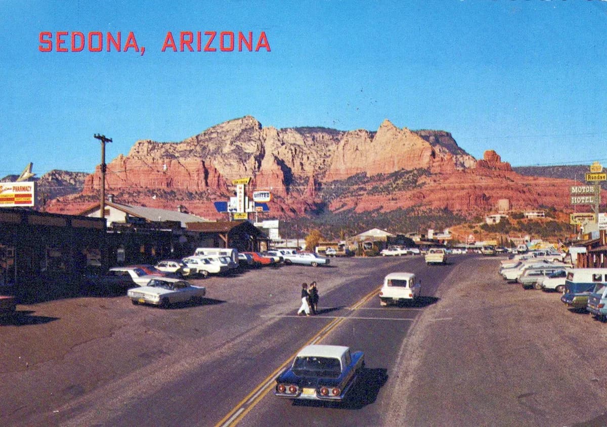 Colour postcard of Uptown Sedona's main street in the early 1970s, with shops, parked cars and red rock cliffs behind