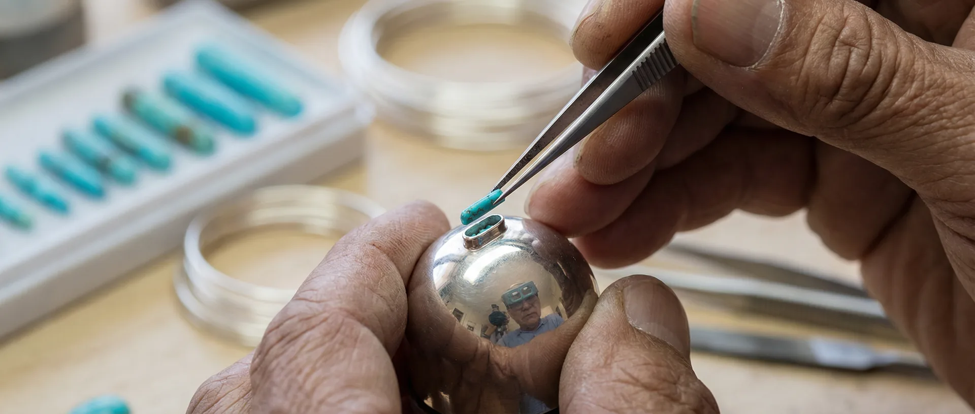 Zuni lapidary hands setting a needle-thin turquoise stone into a silver bezel with fine-tipped tweezers
