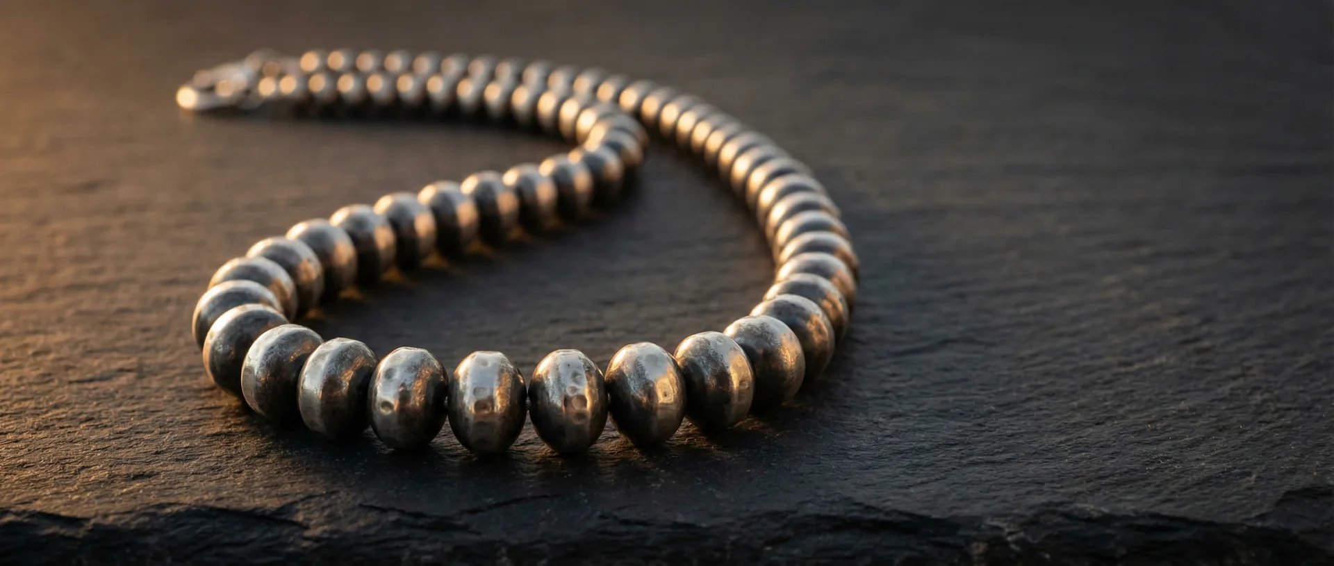 Graduated Navajo pearl necklace draped in an S-curve on dark slate, hand-hammering marks visible on beads